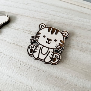 May include: A wooden cutout of a tiger with black stripes. The tiger is sitting with its paws in front of it and has a friendly expression on its face.