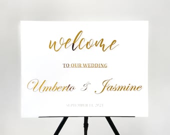 May include: White wedding welcome sign with gold lettering. The sign reads "Welcome to our wedding Umberto & Jasmine September 11, 2021".