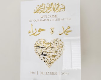 May include: White acrylic wedding sign with gold calligraphy in a heart shape. The sign reads "Welcome to our happily ever after" and includes the date "14th December 2021".