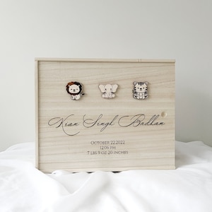 May include: A wooden keepsake box with a lion, elephant, and tiger design. The box is engraved with the name "Kian Singh Badhan", the date "October 22, 2022", the time "12:06 PM", and the weight and length "7 lbs 9 oz 20 inches".
