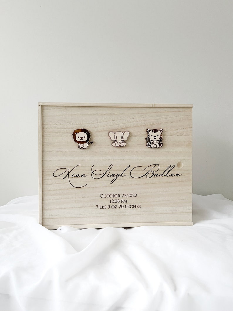 May include: A wooden keepsake box with a lion, elephant, and tiger design. The box is engraved with the name "Kian Singh Badhan", the date "October 22, 2022", the time "12:06 PM", and the weight and length "7 lbs 9 oz 20 inches".