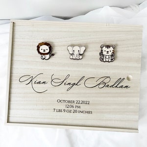 May include: A wooden keepsake box with a light wood finish. The box has a lion, elephant, and tiger design on the front. The box is engraved with the name "Kian Singh Badhan", the date "October 22, 2022", the time "12:06 PM", and the baby's weight and length: "7 LBS 9 OZ 20 INCHES".