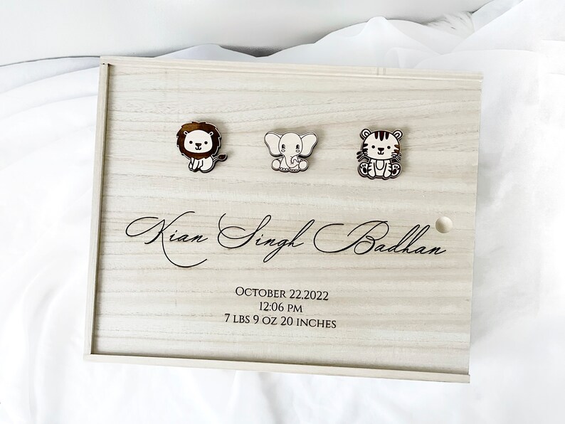 May include: A wooden keepsake box with a light wood finish. The box has a lion, elephant, and tiger design on the front. The box is engraved with the name "Kian Singh Badhan", the date "October 22, 2022", the time "12:06 PM", and the baby's weight and length: "7 LBS 9 OZ 20 INCHES".