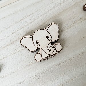 May include: A white wooden elephant with a cute cartoon face and big ears. The elephant is holding a small ball in its trunk.