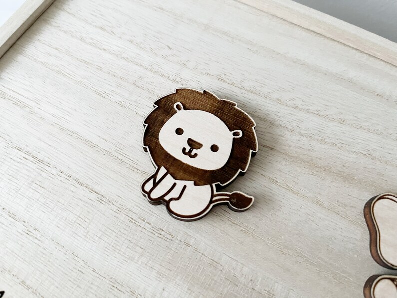 May include: A wooden lion cutout with a brown mane and white face. The lion is sitting with its paws tucked under its body and has a small tail.
