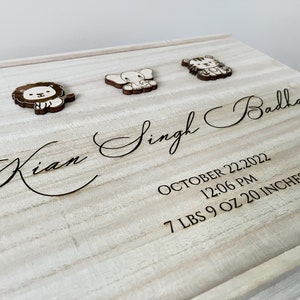 May include: A wooden keepsake box with a light wood finish. The box is engraved with the name "Kian Singh Badhan", the date "October 22, 2022", the time "12:06 PM", and the weight and length "7 LBS 9 OZ 20 INCHES". The box is decorated with three wooden animal cutouts: a lion, an elephant, and a tiger.