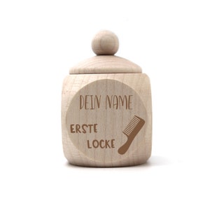Op de afbeelding: Een houten doos met een deksel, gegraveerd met de woorden "DEIN NAME ERSTE LOCKE" en een kam-icoon. De doos is bedoeld om de eerste lok haar van een baby te bewaren.