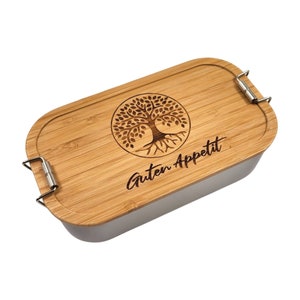 Könnte beinhalten: Eine Holz-Lunchbox mit Edelstahl-Innenraum. Der Deckel ist mit einem lasergravierten Baum des Lebens-Motiv und dem Text "Guten Appetit" versehen.
