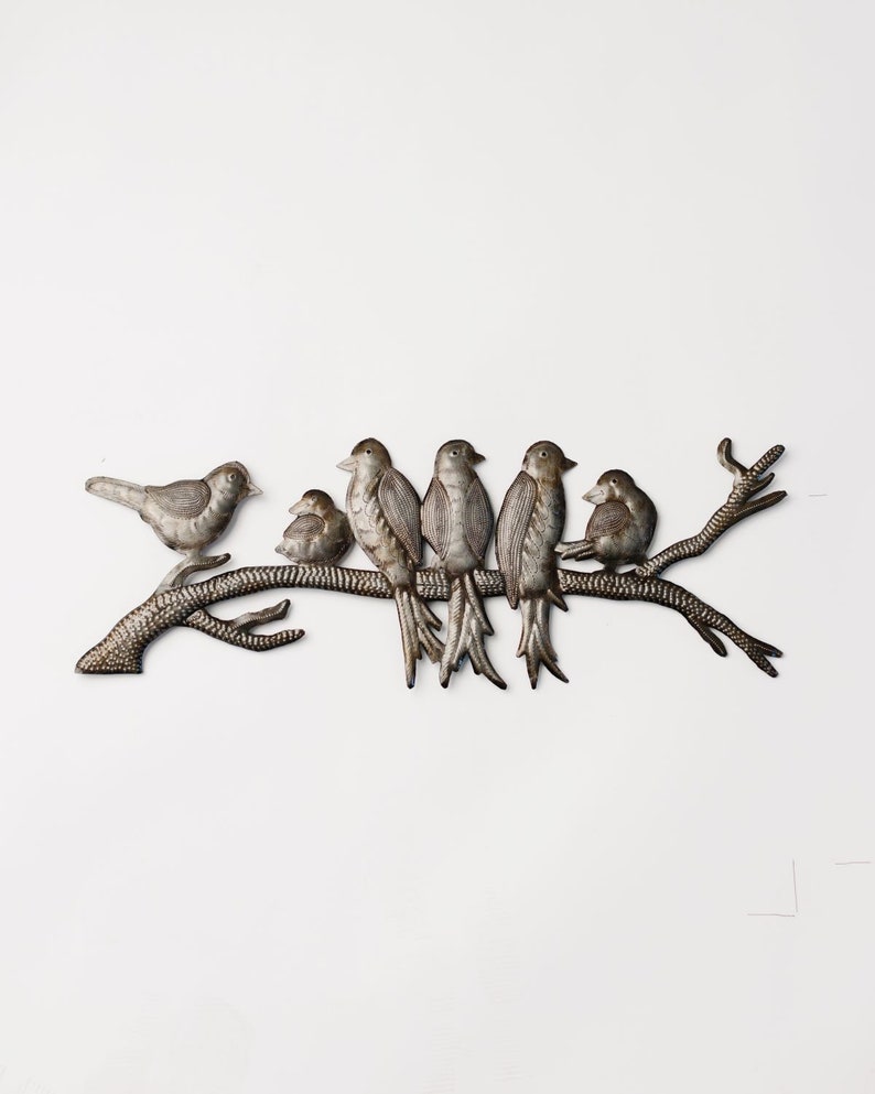 May include: A metal wall art piece featuring six birds perched on a branch. The birds are various sizes and have a metallic finish. The branch is textured and has a naturalistic appearance, creating a nature-inspired decorative element.