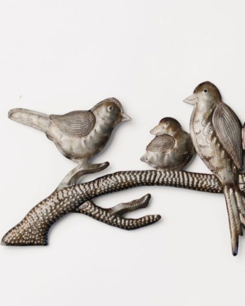 May include: Metal wall art featuring three birds perched on a branch. The birds are silver with detailed feather patterns. The branch is brown with white speckles, set against a white background. A decorative piece for home decor.