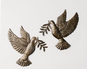 May include: Two metal doves with olive branches in their beaks. The doves are a light gold color and have a textured finish. They are mounted on a white background.