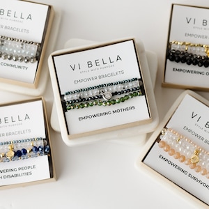 May include: Five boxes of beaded bracelets with gold charms and the text "VI BELLA" and "EMPOWER BRACELETS". Each box features a different color combination and a phrase like "EMPOWERING MOTHERS" or "EMPOWERING SURVIVORS".