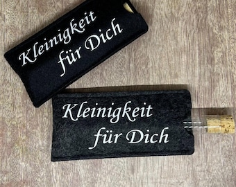 Könnte beinhalten: Zwei schwarze Filztaschen mit weißer Schrift "Kleinigkeit für Dich". Eine Tasche ist offen und enthält ein kleines Glasröhrchen mit Korken. Die andere Tasche ist geschlossen. Auf einer Holzoberfläche.