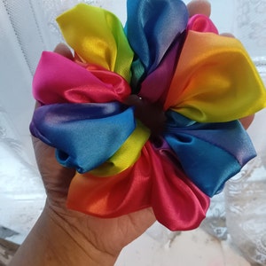 Puede incluir: Un scrunchie de satén con colores de arcoíris con un degradado de colores, incluyendo rojo, naranja, amarillo, verde, azul, índigo y violeta.