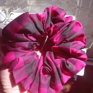 Könnte beinhalten: Ein rosa-schwarzes Karostoff-Haargummi. Das Scrunchie ist aus Stoff und zu einem Kreis zusammengezogen.