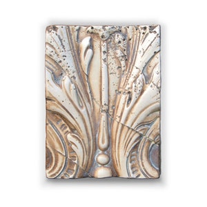 Könnte beinhalten: Eine dekorative Keramikfliese mit einem erhabenen Design aus stilisierten Blättern und einem zentralen Motiv. Die Fliese ist in Beige- und Brauntönen gehalten und hat einen abgenutzten, antiken Look.