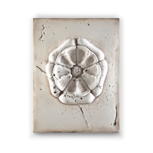 Könnte beinhalten: Eine weiße Keramikfliese mit einem erhabenen, geprägten Blumendesign. Die Fliese hat einen abgenutzten, antiken Look.