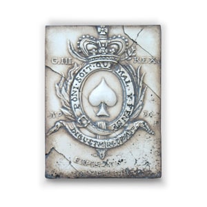 Könnte beinhalten: Eine weiße Keramikfliese mit einem erhabenen Design einer Krone, einer Pik und einem Banner mit dem Text "DIEU ET MON DROIT". Die Fliese trägt außerdem den Text "G. III. REX" und "HONI SOIT QUI MAL Y PENSE".