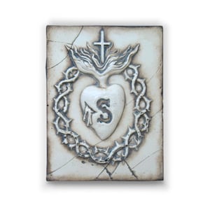 Könnte beinhalten: Eine weiße Keramikfliese mit einem erhabenen Bild eines Herzens mit einer Dornenkrone, einem Kreuz und dem Buchstaben "S" in der Mitte. Die Fliese hat einen abgenutzten, antiken Look.