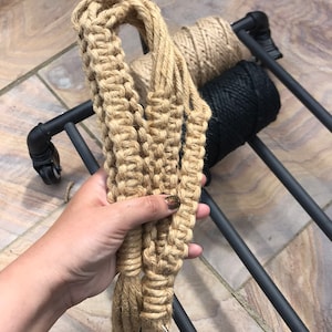 May include: A close-up of a hand holding a thick, natural fiber rope with a silver ring at the end. The rope is coiled and appears to be handmade.