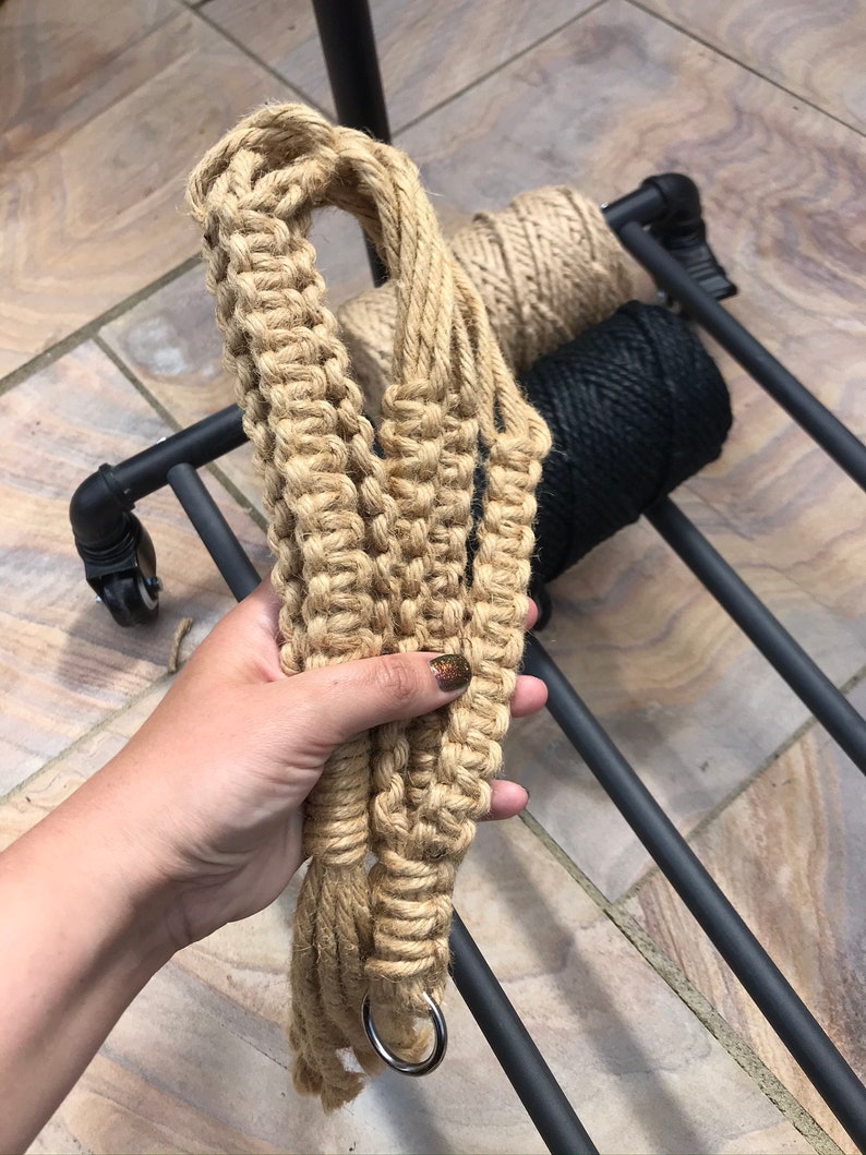 May include: A close-up of a hand holding a thick, natural fiber rope with a silver ring at the end. The rope is coiled and appears to be handmade.