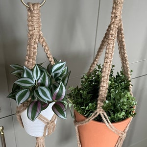 May include: Two macrame plant hangers with pots and plants. The plant hangers are made of natural jute rope and have a simple design. One plant is in a white pot and the other is in a terracotta pot.