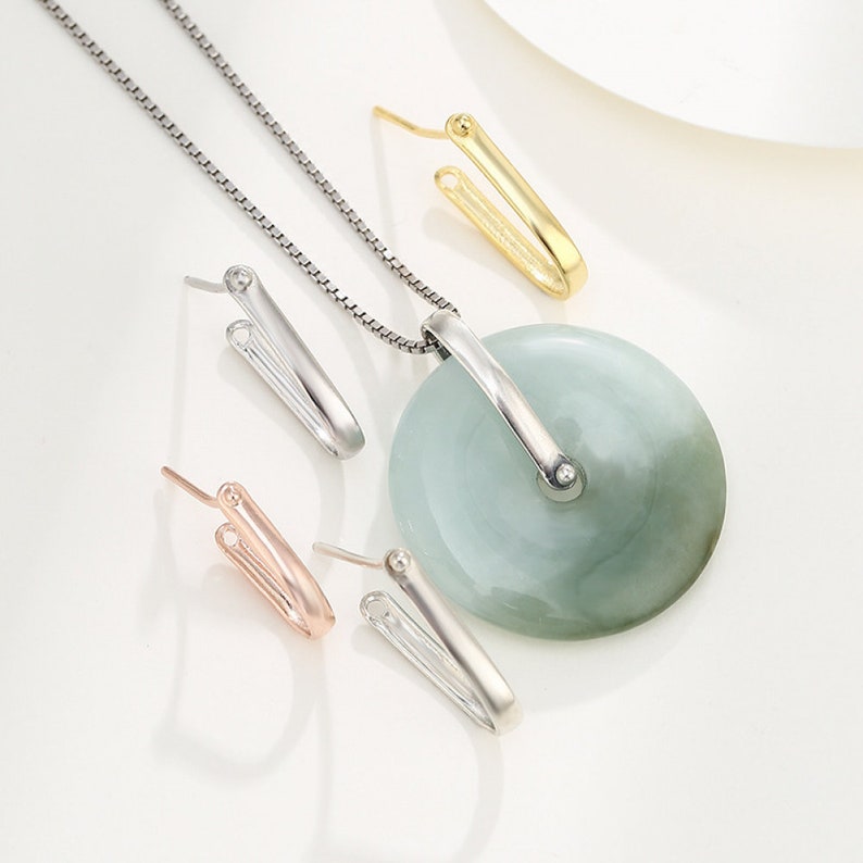 May include: A set of three silver-toned pendant clasps, one gold-toned pendant clasp, and a jade pendant with a silver-toned chain. The pendant clasps are shaped like a V and have a small ball at the top.