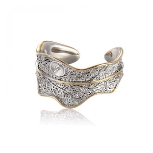 Puede incluir: Un anillo de plata y oro en forma de hoja con un diseño delicado. El anillo es abierto y ajustable.