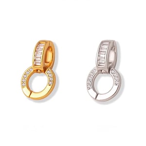 Puede incluir: Dos pendientes, uno dorado y otro plateado, cada uno con un diseño circular con pequeñas piedras transparentes y un acento de piedra rectangular. Los pendientes se muestran sobre un fondo blanco.