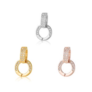 Könnte beinhalten: Drei Anhänger in verschiedenen Metalloberflächen: Silber, Gold und Roségold. Jeder Anhänger hat ein Doppelkreisdesign mit einer Reihe von klaren Zirkonia-Steinen um jeden Kreis.