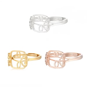 May include: Three rings with a square-shaped design featuring a decorative cutout of a stylized butterfly. The rings are shown in silver, gold, and rose gold.