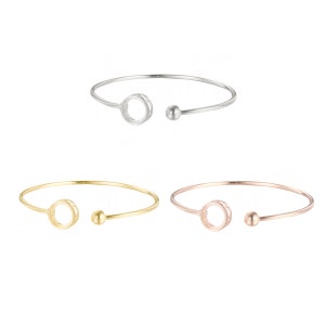 May include: Three open circle bangle bracelets in silver, gold, and rose gold. Each bracelet has a small ball at the end.