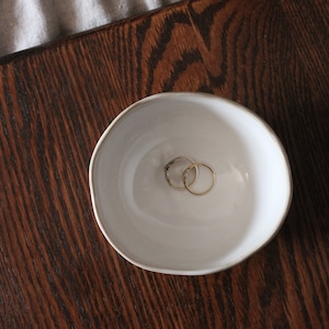May include: Two gold rings in a white ceramic bowl on a dark wood surface.