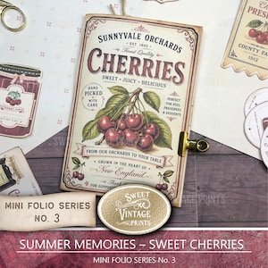 May include: A rectangular paper folio featuring a vintage-style label for Sunnyvale Orchards Cherries. The design includes a central illustration of red cherries on a branch, decorative typography, and a gold metal clip attached to the right edge.