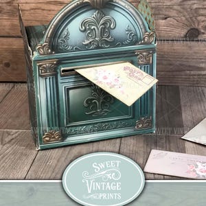 Peut inclure: Une boîte aux lettres de style vintage, de couleur sarcelle et dorée, avec un dessus en forme d'arche décorative. Une carte postale avec des motifs floraux est dans la fente. Le texte "Sweet Vintage Prints" et "Vintage Valentine's Mailbox".