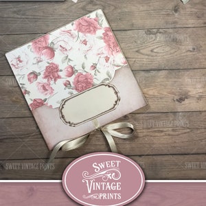 Op de afbeelding: Een roze en wit bloemenpatroon junk journal folio met een beige lint en een label. De folio ligt op een houten oppervlak. De tekst "Sweet Vintage Prints" en "Vintage Peonies Folio" is zichtbaar op de afbeelding.