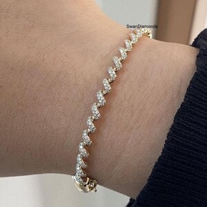 May include: A gold bracelet featuring a continuous, repeating zigzag or wave-like pattern encrusted with small, clear pavé-set diamonds. The piece includes a secure clasp mechanism and displays the text SwanDiamonds near the top edge.