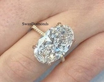 May include: A large oval-shaped diamond engagement ring set in a gold band. The ring is on a finger with white nail polish.