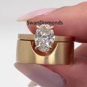 Puede incluir: Un juego de anillos de oro con un diamante ovalado solitario. El diamante está engastado en una banda de oro, y el juego incluye una banda de oro a juego. La marca "SwanDiamonds" es visible.