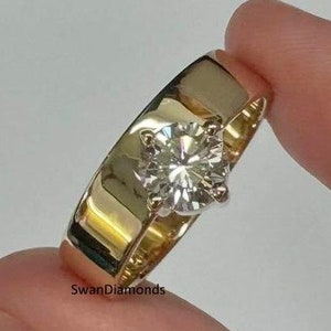 Op de afbeelding: Een gouden verlovingsring met een grote, ronde, heldere diamant in het midden. De ring zit aan een vinger.