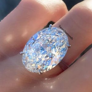 May include: A large, oval-shaped diamond ring set in a white gold band. The diamond is clear and sparkling, and the ring is on a finger.