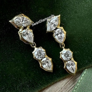 May include: A pair of gold earrings with pear-shaped and round diamonds. The earrings are dangling and have a delicate design.