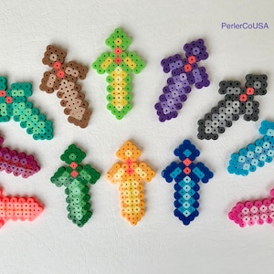 May include: A collection of colorful cross-shaped Perler bead crafts in various colors, including green, brown, purple, and blue. Each cross has a unique design and color scheme, with a small accent bead in the center. The text "PerlerCoUSA" is in the top right corner.