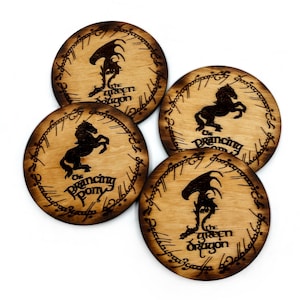Peut inclure: Quatre dessous de verre en bois de couleur marron clair. Chaque dessous de verre présente une silhouette noire d'un dragon ou d'un cheval, avec du texte du Seigneur des Anneaux. Les dessous de verre sont ronds et ont une bordure marron foncé.