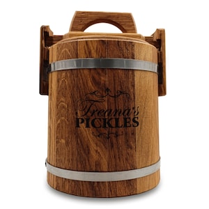 May include: A wooden pickle barrel with a handle and metal bands. The barrel has the text "Treana's PICKLES" in a decorative font. The wood grain is visible, and the barrel is cylindrical.