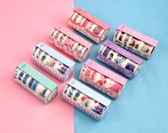May include: Set of six colourful washi tape rolls with various floral and geometric patterns. Each roll is packaged in a cardboard box with a matching design. The boxes are arranged in a row on a pink and blue background.