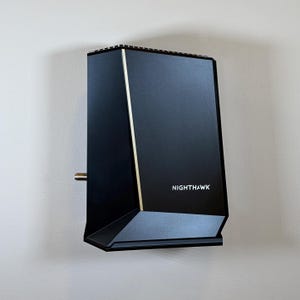May include: A black, wall-mounted electronic device with gold trim and the word "NIGHTHAWK" in white lettering. The device has a geometric design and a silver port extending from the side.