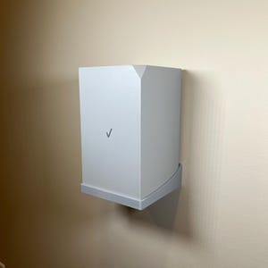 May include: A white wall-mounted router with a checkmark logo. The router has a rounded edge and a white wall mount.
