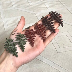 Può includere: Tre paia di orecchini a forma di felce realizzati con macramè. Gli orecchini sono in tonalità di verde, marrone e ruggine.