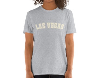 May include: A heather grey t-shirt with the text "LAS VEGAS" in a cream coloured, varsity-style font.